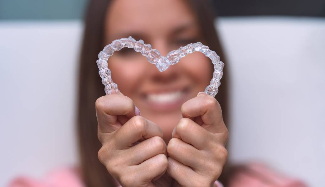 Woman smiling while holding her aligners in a heart shape